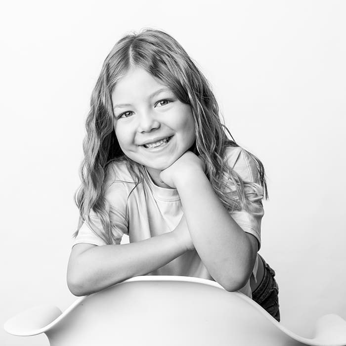 black and white portrait of girl leaning on chair with chin on her hand