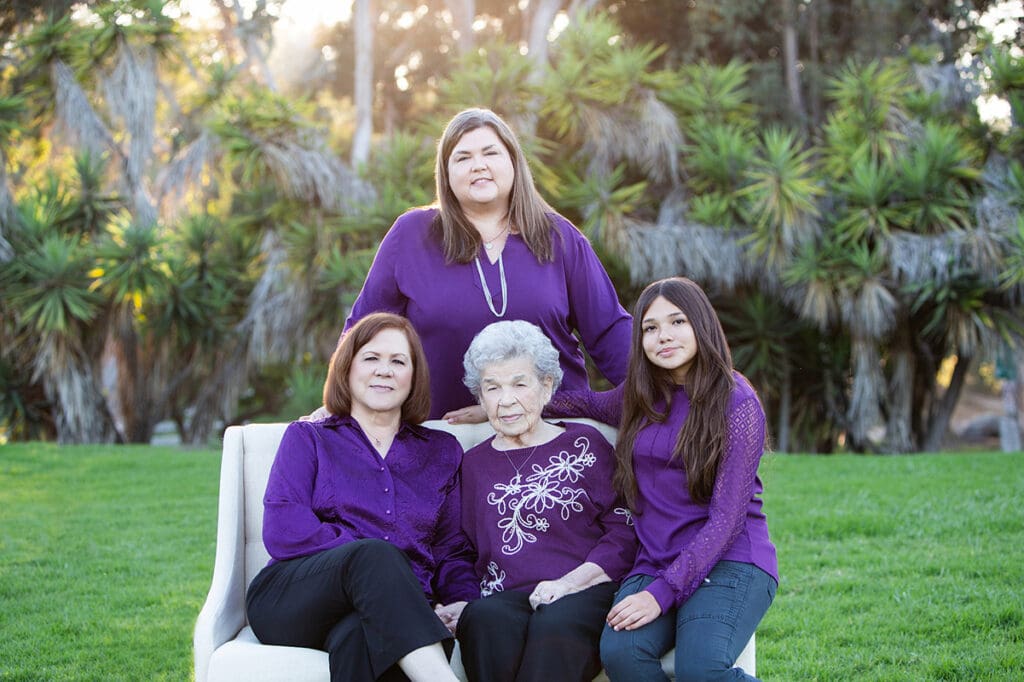 generational portrait of grandkid with grandma and great grandma in a park on a sofa wearing purple